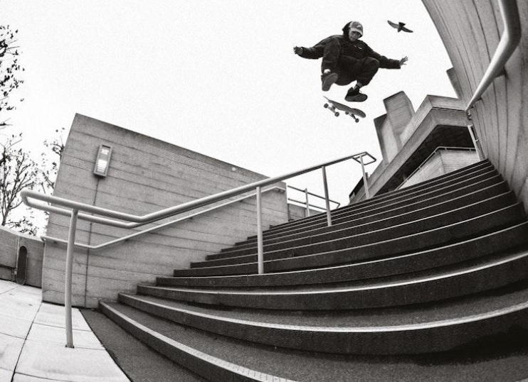 Black and white photo of a skateboarder doing a trick over a large stair set